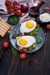 Fried eggs, bacon and cream cheese sandwiches on a plate on wooden table at domestic kitchen