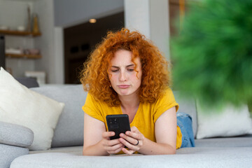 Woman using mobile phone while lying on sofa. Young female is resting at home.