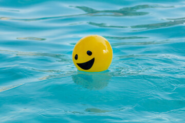 Pelota amarilla con una cara sonriendo flotando sobre el agua azul