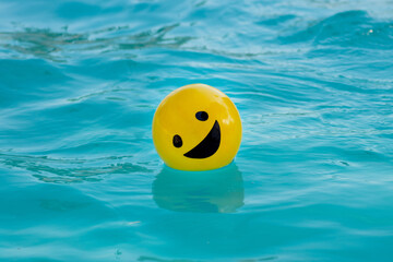 Pelota amarilla con una cara sonriendo flotando sobre el agua azul