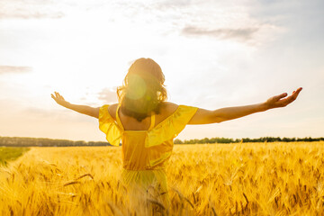 Young woman in yellow dress standing on a wheat field with sunrise on the background