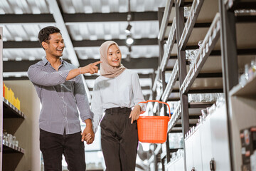 Asian Muslim young couple carrying baskets while looking at glassware in houseware store