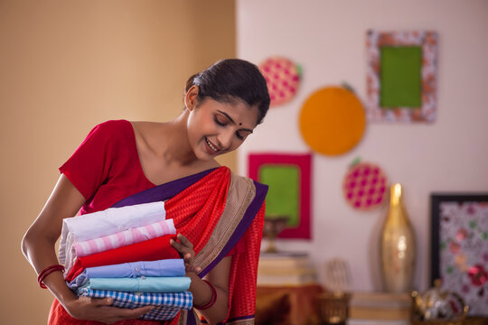Portrait of cheerful woman holding neatly folded stack of clothes