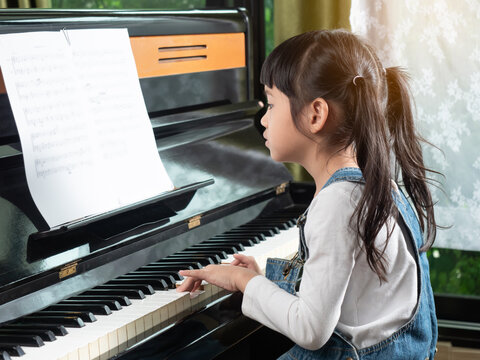 Asian little girl practice play piano in house. Cute kid learning to play piano. - Powered by Adobe