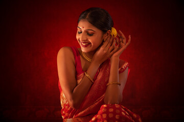 Smiling Indian woman in traditional outfit adjusting flower in her hair against red background