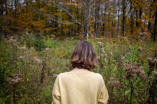 Short haired woman in yellow shirt walks through unkempt rustic woodland landscape in fall foliage 