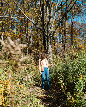 Vertical shot of stylish person in vintage jacket touching flora in wild fall idyllic landscape in upstate New York