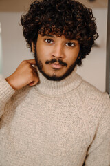 Portrait of young handsome indian curly man in sweater