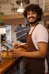 Fototapeta na wymiar Young indian smiling handsome curly barista working with tablet