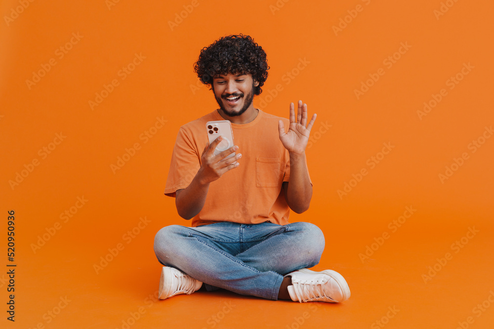 Wall mural young handsome indian smiling man sitting with phone