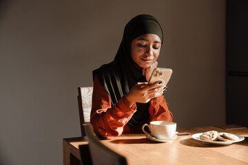 Young beautiful calm woman in hijab sitting at kitchen table