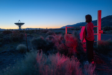 Curious stargazer and astronomy buff ponders alien life in film noirish red light explores radio observatory in dark sky