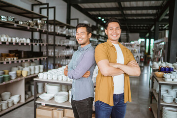 Handsome smiling asian man standing with hands crossed in ceramic glassware shop