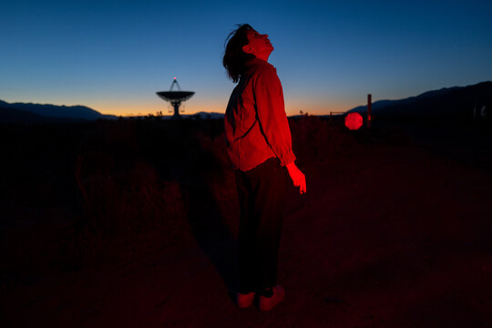 Curious stargazer and astronomy buff ponders alien life in moody red light explores radio observatory in dark sky