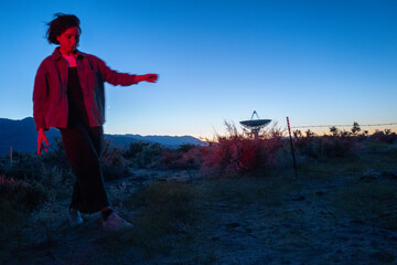 Curious stargazer and astronomy buff ponders alien life in film noir red light near radio observatory under dark sky