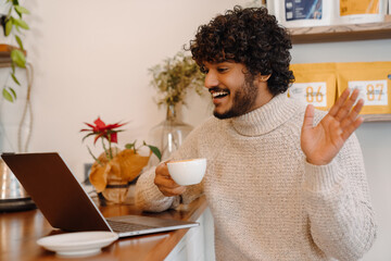 Fototapeta na wymiar Young smiling handsome indian curly man holding videoconference with laptop