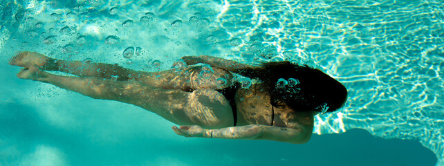 Woman swimming underwater in a blue pool. - 520951741