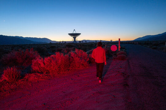 Curious stargazer and astronomy buff ponders alien life in moody red light explores radio observatory in dark sky