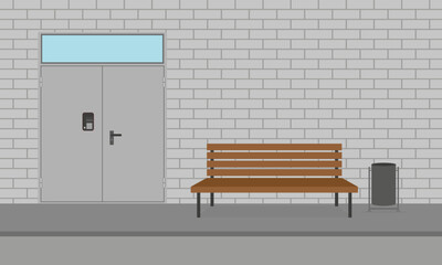 Metal door with intercom,wooden bench and trash can on sidewalk against the backdrop of a brick wall