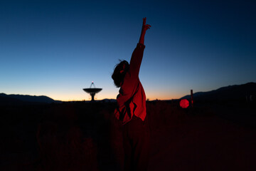 Intellectual stargazer and astronomy buff points at stars in moody red light near radio observatory under dark sky