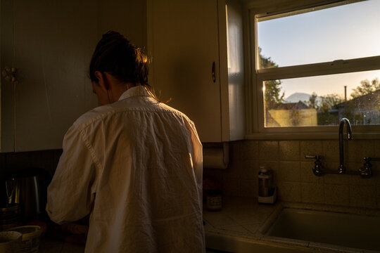 a home chef works in the kitchen in golden hour light by a window sill 