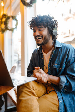 Young smiling handsome indian curly man holding videoconference with laptop