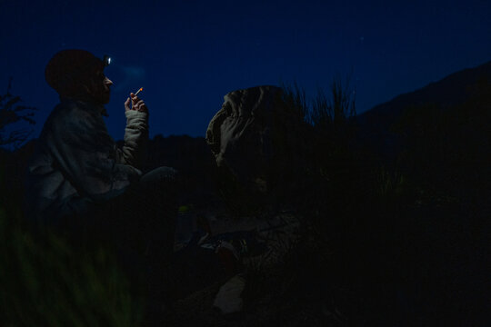 Person with headlamp smokes under starry night sky