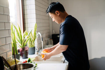 Adult asian man washing vegetables in cozy kitchen