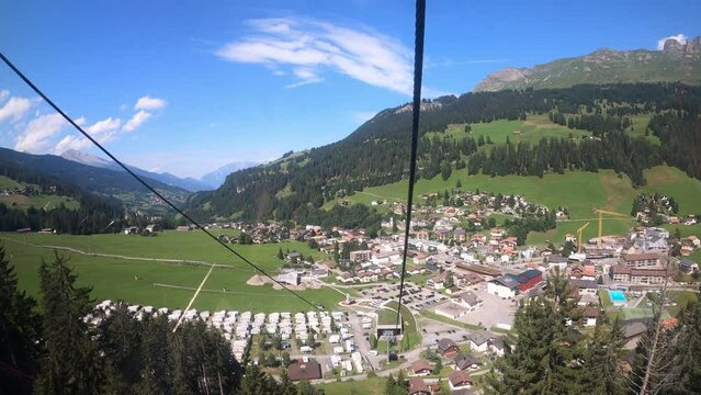 Cable car ride in Switzerland. The cable car descends into the valley. You can see the small village in the valley and the beautiful nature of Switzerland with its hiking trails. Grisons