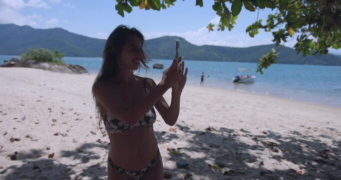 Young mother on tropical beach taking photos with smart phone - side profile