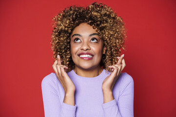 Young black woman with afro curls smiling and holding fingers crossed