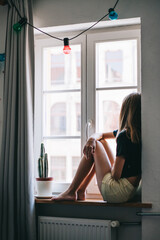 The girl is sitting in the room on the windowsill.