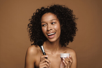 Black shirtless woman using powder brush while doing makeup
