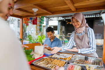 Fototapeta na wymiar muslim couple ordering food to break fasting in traditional food market stall served by the seller