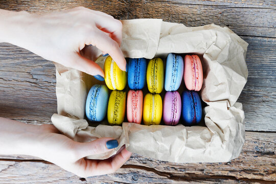 Female hand taking macaron from the package. Top view.