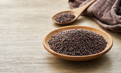 black mustard seed in wood plate and spoon on wooden table background. a pile of black mustard seed in wood plate on wooden table background.                                       