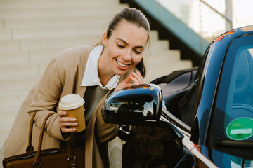 Young woman smiling and drinking coffee while standing by her car