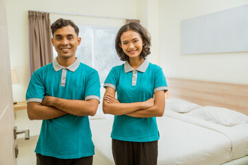 two janitors wearing turquoise uniforms smiling while standing with their arms crossed in a hotel...