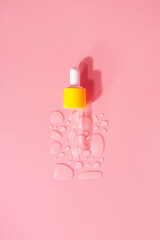 Bottle of drops of anti-aging emulsion and glass pipette on light pink surface close upper view....