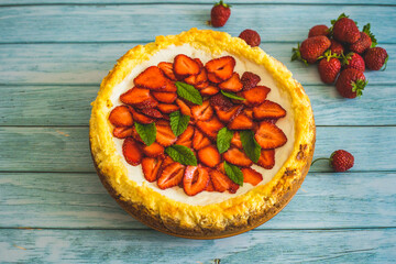 Strawberry homemade cake on wooden table.Delicious cheesecake with strawberries decorated with mint leaves.Top view.Healthy organic summer berry dessert.Perfect cake for a birthday