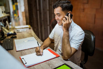receptionist takes a phone call and takes notes on paper while sitting at the hotel reception desk