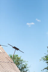 An old antenna on the roof against a blue clean sky with parts of the trees on the background