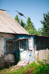 An old abandoned village house with a number 49 on a sign. A blue door entrance and an old antenna on a roof