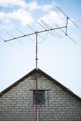 An old antenna on the roof against a blue c;oudy sky. A small old window is on the center of the frame