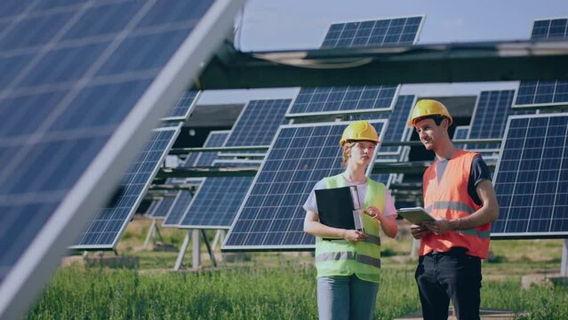 Two technician lady and man analysing together and discussing about cleanliness of photovoltaic solar panels they standing in the middle of solar power farm