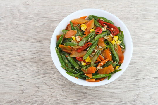 Orak arik sayur or stir fried vegetables with carrot, bean, corn and egg. Served in white bowl on wooden background. 