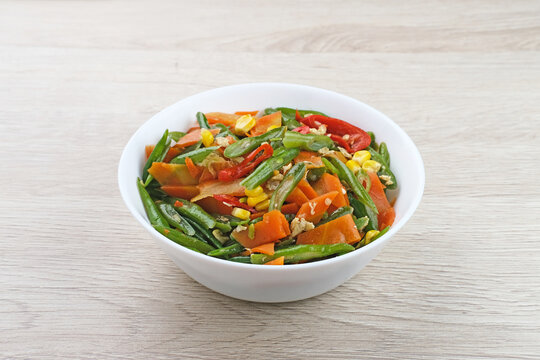 Orak arik sayur or stir fried vegetables with carrot, bean, corn and egg. Served in white bowl on wooden background. 