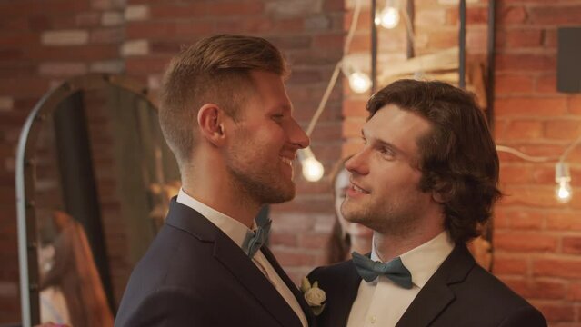 Waist up slowmo of newlywed romantic gay couple looking at each other and dancing in front of friends holding sparklers, having lgbtq wedding party