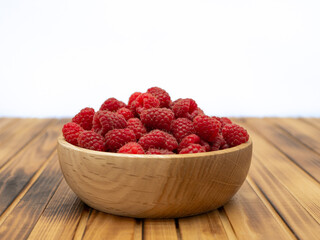 Fresh raspberries in wooden bowl on wooden background. With copy space for text
