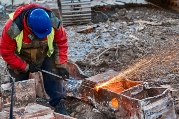 Worker in helmet cuts old metal beam for recycling at site